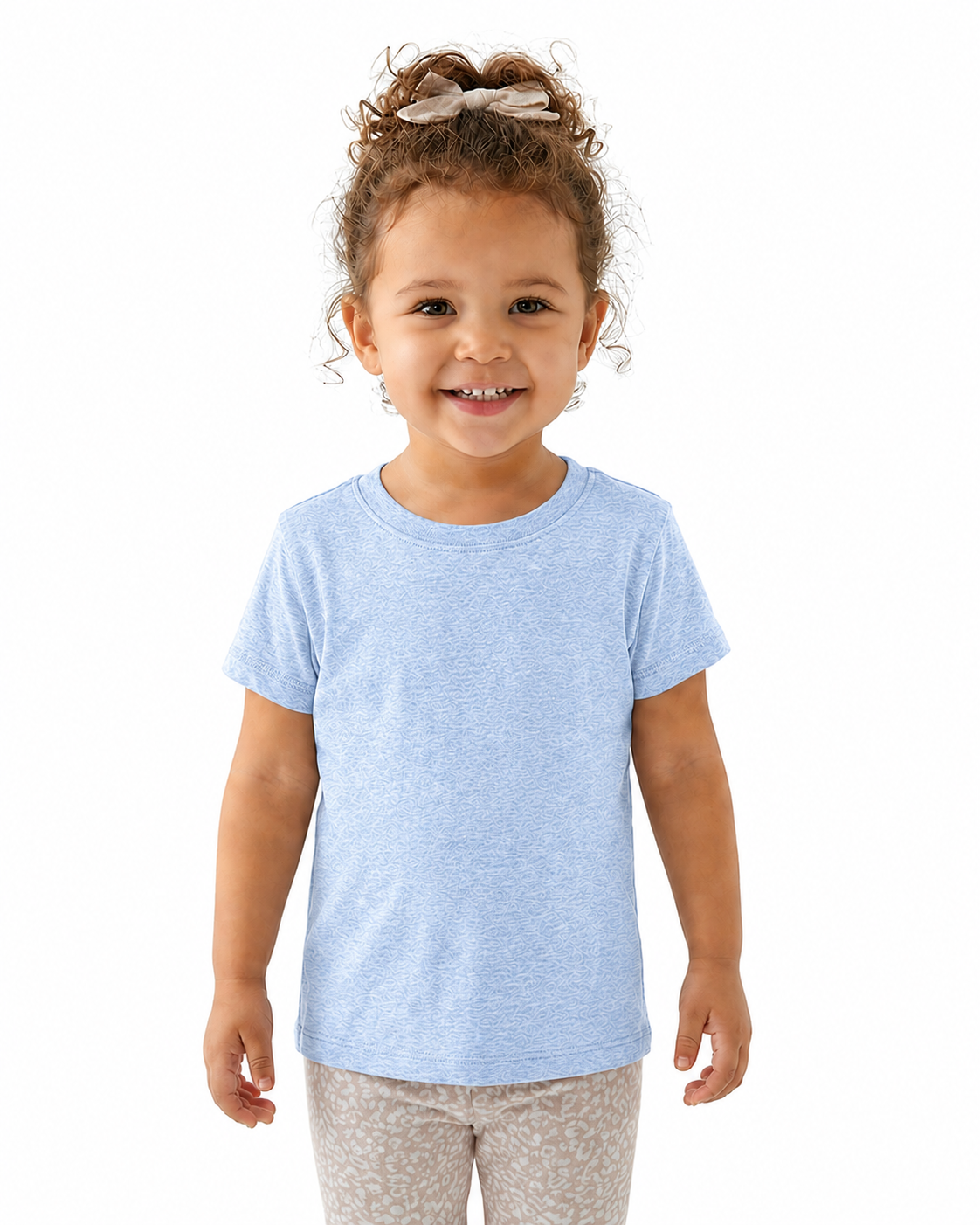 A young child with curly brown hair wearing a light blue short-sleeve crewneck t-shirt and patterned leggings, standing against a solid white background.