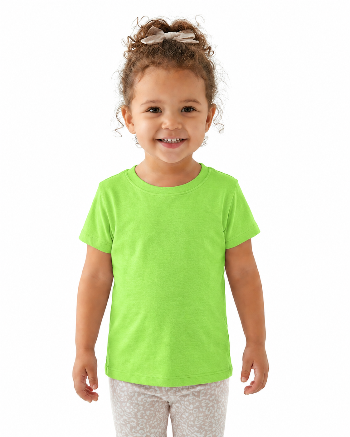 A young child with curly brown hair wearing a bright lime green short-sleeve t-shirt and light gray patterned pants, standing against a solid white background.