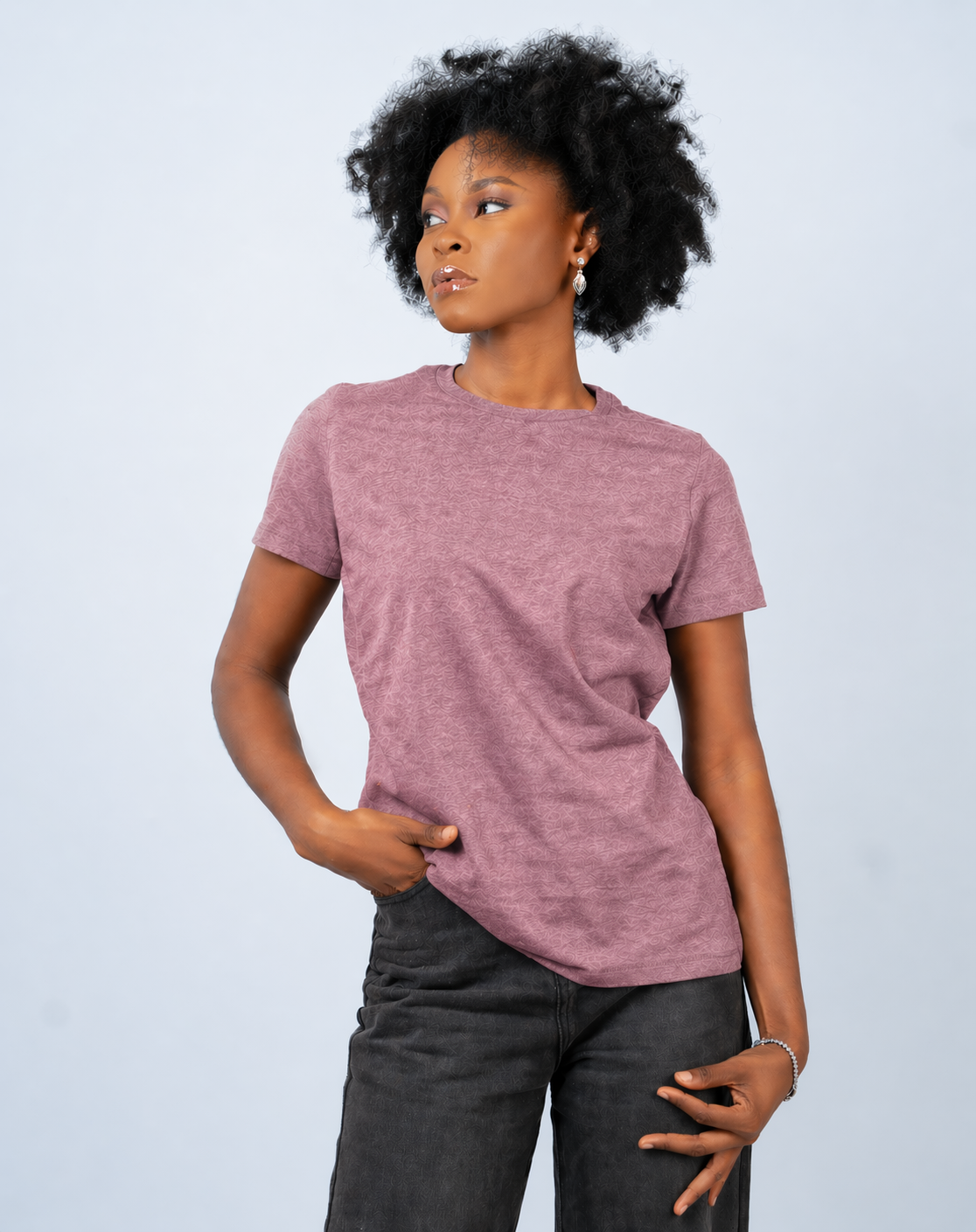 Person wearing a mauve t-shirt and dark pants against a light gray background