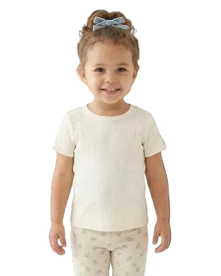 Young girl wearing a white ribbed t-shirt and light-colored pants with a subtle pattern on a white background