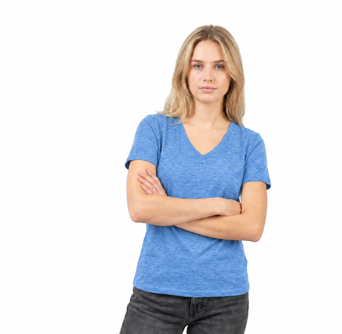 A woman with blonde hair wearing a heather blue v-neck t-shirt and dark gray jeans, standing with her arms crossed against a solid white background.