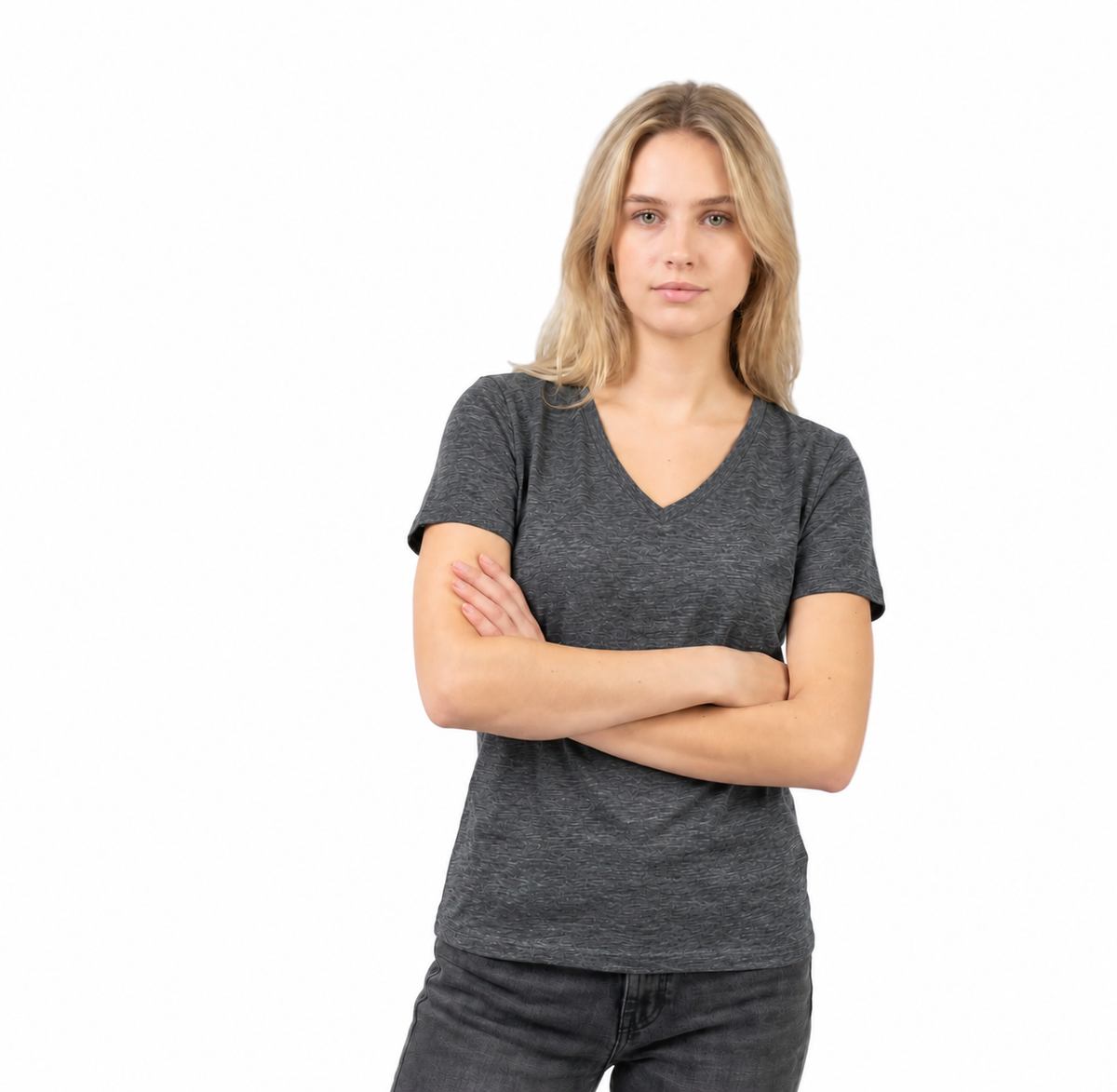 A blonde woman with her arms crossed stands against a solid white background, wearing a dark gray heathered v-neck t-shirt and dark gray jeans.