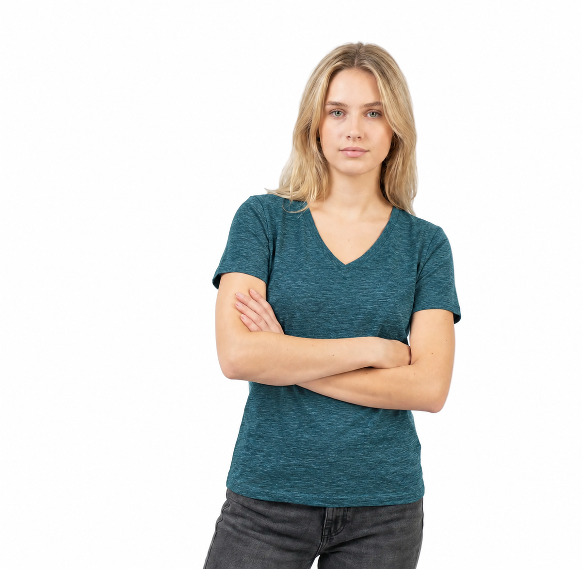 A woman with blonde hair wearing a teal heathered v-neck t-shirt and dark gray jeans, standing with her arms crossed against a solid white background.