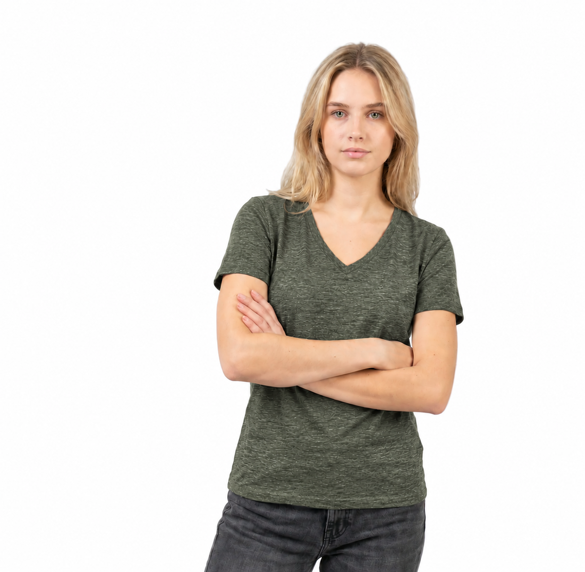 A woman with blonde hair wearing a dark olive green heathered v-neck t-shirt and dark gray jeans, standing with her arms crossed against a solid white background.