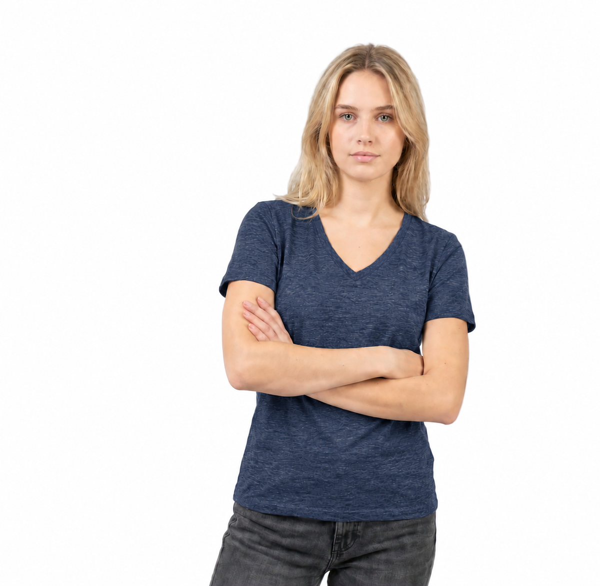 A woman with blonde hair wearing a heathered navy blue v-neck t-shirt and dark gray jeans, standing with her arms crossed against a solid white background.