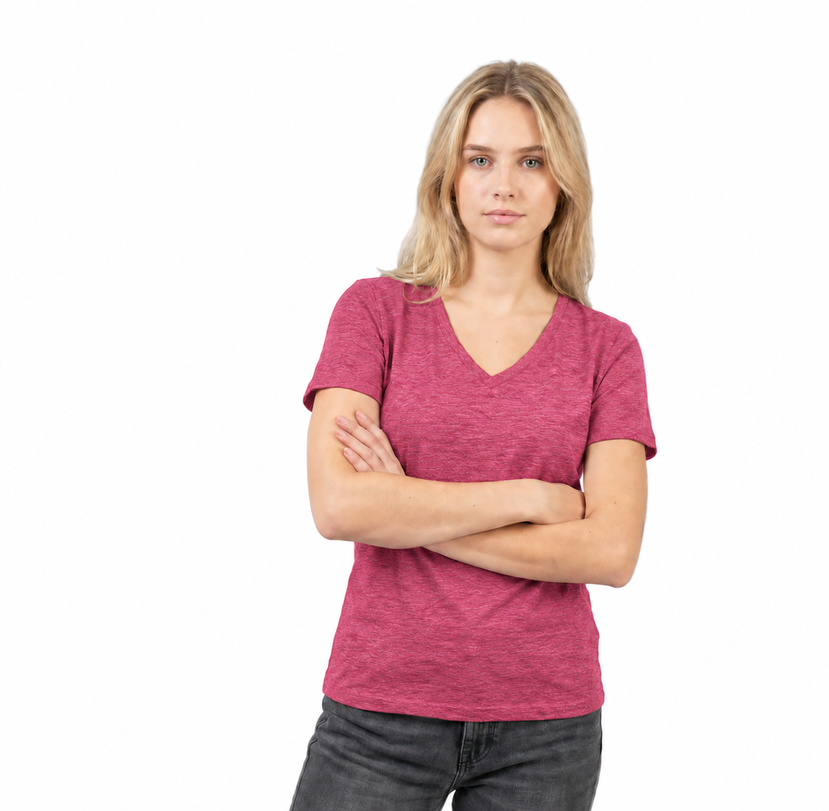 A woman with blonde hair wearing a heathered pinkish-red v-neck t-shirt and dark gray jeans, standing with her arms crossed against a solid white background.