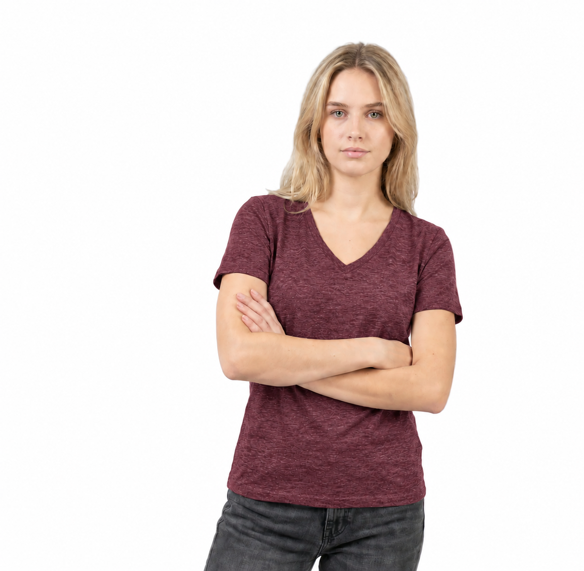 A woman with blonde hair wearing a heathered burgundy v-neck t-shirt and dark gray jeans, standing with her arms crossed against a solid white background.