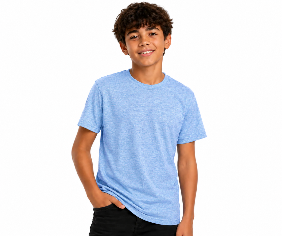 A smiling young man with curly brown hair wearing a light heather blue crewneck t-shirt and black pants, standing against a solid white background.